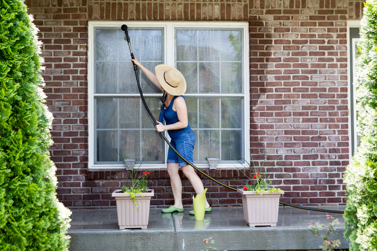 Woman cleaning exterior windows of home. Zenith Properties NW in Clark County WA shares some helpful spring home maintenance tips.